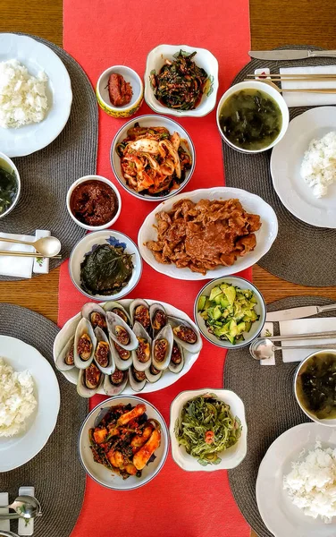 Table with red cloth and crockery set for four guests with asian food ready-to-eat