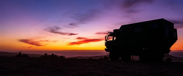 Silhouette of RV motorhome camping truck in front of colorful sunset, Sahara Desert, Morocco