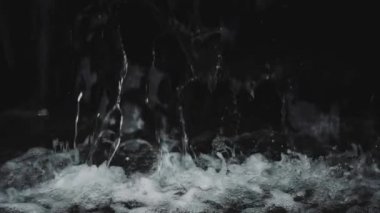 Şeffaf suyun aktığı ve siyah arkaplana karşı yavaş çekimde sıçrayan soyut arkaplan