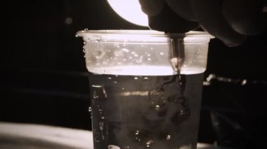 Tanımlanamayan bir dövme ustası su dolu bir kaba iğne batırıyor ve siyah mürekkeple yıkıyor.