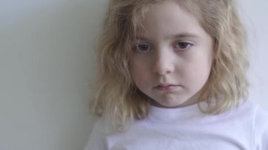 Sıradan tişörtlü küçük bir çocuk stüdyoda beyaz arka planda kameraya bakıyor.