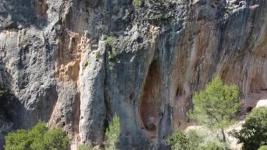 Güneşli bir günde yüksek dağın kayalık yamacında tırmanan halat ve güvenlik ekipmanlarıyla aktif kadın dağcı drone görüntüsünden.