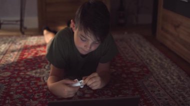 Haftasonu evde günlük giysiler içinde, kulaklık takıp laptopunu karıştıran düşünceli bir çocuk.