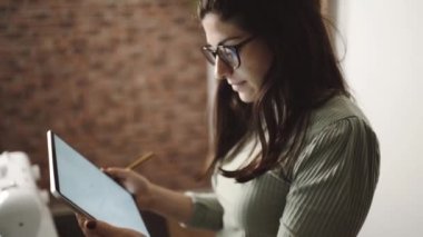 Yukarıdan gelen terzi, tablet kullanırken öne eğildi ve stüdyodaki kağıtları masaya koydu.