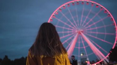 Aydınlatılmış iskelede yürüyen genç bir turist Montreal 'de arka planda parlayan dönme dolaba bakıyor.