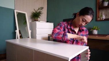 Etnik Asyalı kadın evde yeni mobilya montajı yaparken yerde oturuyor ve tahta tahtayla düzüşüyordu.