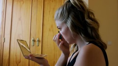 Renkli göz farı ve ayna ile palet tutan genç bir kadın ve evde güzellik prosedürü sırasında kirpiklerine siyah rimel sürüyor.