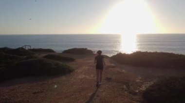 Spor kadını silueti, antrenmandan sonra huzurlu gün batımında deniz manzarasına hayran.