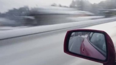 Kırsal kesimde kış günü, karlı köy ve ormanlarda hızla ilerleyen modern kırmızı otomobilin penceresinden yansıyan hızlandırılmış manzara dikiz aynasına odaklanıyor.