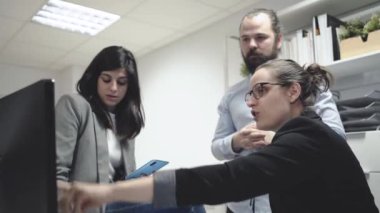 Ciddi genç iş adamları ve bayan meslektaşlar bilgisayar etrafında toplanıp iş verilerini tartışırken çağdaş çalışma alanında birlikte çalışıyorlar.