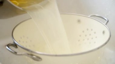 Kimliği belirsiz bir erkeğin mutfakta makarna hazırlarken tavadan kevgire sıcak spagetti dökmesi yakın plan.