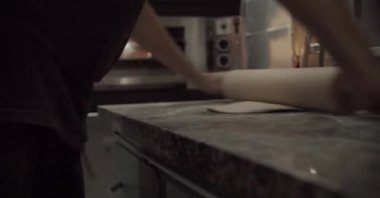 Mutfakta pizza hazırlarken masaya taze hamur germek için merdane kullanan isimsiz bir adam.