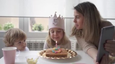 Evde doğum gününü kutlarken anne ve kızının günlük kıyafetlerini giyip birlikte oturup tablet üzerinde video görüşmesi yapmaları.