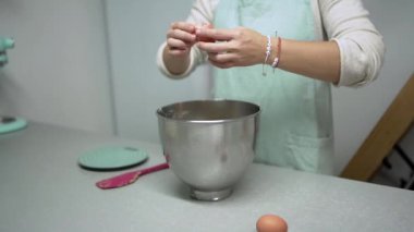 Kimliği belirsiz kadın pastacı mutfakta tatlı hazırlarken çelik kaseye yumurta kırıyor.