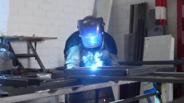 Fabrikadaki tezgahta çalışırken kaynak makinesi kullanan tanınmayan bir erkek kaynakçı.