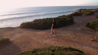 Huzurlu bir gün batımında koştuktan sonra dinlenirken deniz manzarasına hayran olan sporcu kadın.