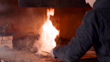 Sıradan giysiler içinde kömür ocağı yangınını sürdüren kimliği belirsiz genç demirci.