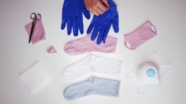 Koronavirüs karantinası sırasında maske yapmak için çorap, akıllı telefon, peçete, maske ve makas yanında mavi eldiven takan tanınmayan kişilerin üst görüntüsü.
