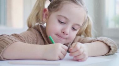 Hafif anaokulunda masada otururken günlük kıyafet çizen sevimli çocuk.