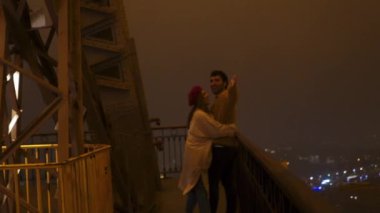 Paris 'te sonbahar tatilleri boyunca Eyfel Kulesi' nin gözlem güvertesinden sisli geceleri izleyen romantik çok ırklı çift.