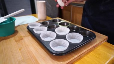 Kek tepsisi ve kağıt kaplamalarla masada duran önlüklü tanınmamış bir insan yemek pişirmek için bulaşık takımını hazırlarken...