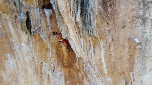 日当たりの良い日に高い山の岩の斜面を登るロープや安全装置とスポーツウェアのアクティブな女性の登山者のドローンビューの上から — ストック動画