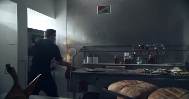 隐姓埋名的厨师拿着金属铲子拿着意大利传统的生食披萨从大理石台面烤成烤箱在餐馆厨房里烤 — 图库视频影像