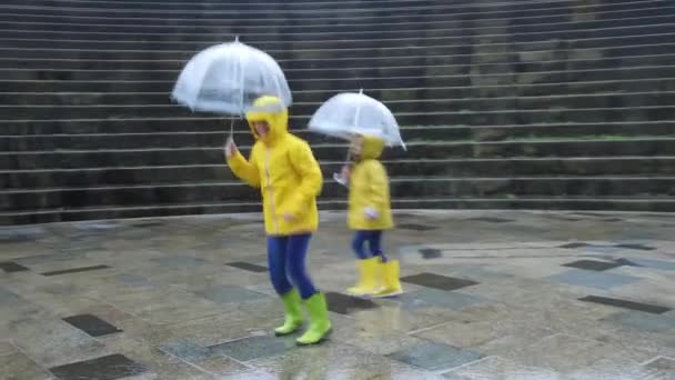 Elragadó Testvérek Sárga Esőkabátban Gumicsizmában Esernyőkkel Kezükben Élvezik Nedves Utcát — Stock videók