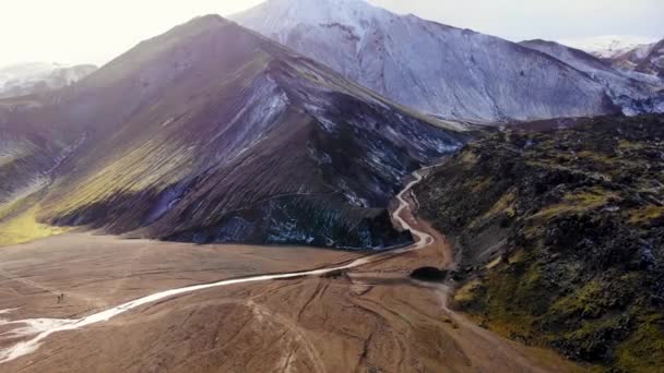 アイスランドの晴れた日に壮大な雪の山の尾根に流れる狭いストリームのドローンビューの周りパン — ストック動画