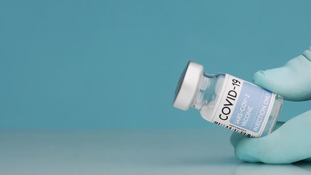 作物の閉鎖認識できない医師で手袋充填注射器でワクチンでコロナウイルスからガラス瓶の青の背景に — ストック動画