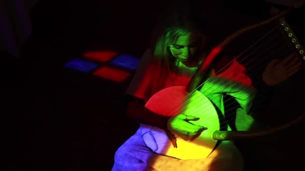 Góry Blondynka Gra Tradycyjną Muzykę Lirze Siedząc Pokoju Wielobarwnym Oświetleniem — Wideo stockowe