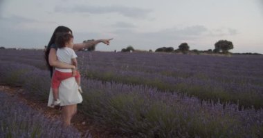 Mor lavanta çiçekleriyle çiçek açan tarlada durup günbatımının tadını çıkarırken kucağında çocuğu tutan, tanınmayacak kadar sevecen bir annenin yan görüntüsü.