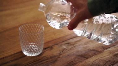 Kimliği belirsiz erkek bardağı plastik şişeden taze maden suyuyla dolduruyor.
