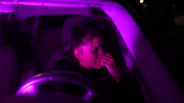 Genç ve üzgün bir kadın sürücünün gece yolunda arabada otururken kişisel sorunlarından dolayı ağlaması ön camdan dışarı yansıyor.