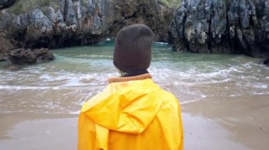 Sarı yağmurluk giyen, Cobijero Sahili 'nin taşlı sahillerinde dinlenen ve sonbaharda bulutlu bir günde göl manzarasına hayran olan tanınmamış kadın kaşifin arka planı.