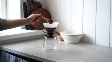 Ahşap kaşıkla kesilmiş, kağıt filtreye öğütülmüş kahve ekleyerek aromatik içeceği hazırlayan kişi.
