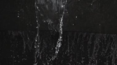 Şeffaf suyun aktığı ve siyah arkaplana karşı yavaş çekimde sıçrayan soyut arkaplan
