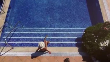 Yüzme havuzunun yukarısından, havuz kenarında tanınmayan bir kadın, havuz kenarında dinlenirken oğlu da yaz tatilinde suya atlayıp yüzüyor.