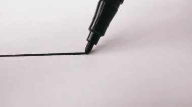 Siyah keçeli kalem ucu beyaz yüzeyde düz çizgi çiziyor.