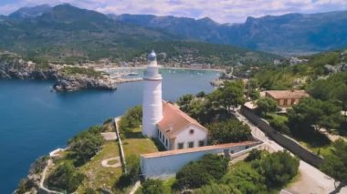 Yeşil kayalık tepeleri ve sahil kenarında beyaz deniz feneri olan küçük yerleşim yerlerini gösteren drone görüntüsünü yakınlaştır.