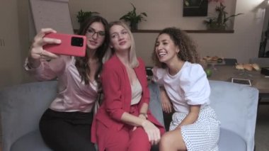 İş konferansında gülümseyen ve selfie çeken şık giyimli iş kadınları.