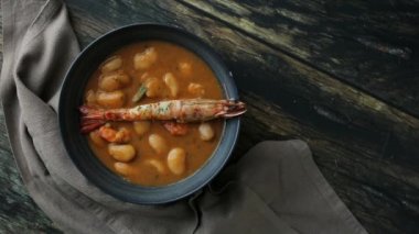 Beyaz fasulye ve Langoustines ile aperatif krema çorbasının yukarısından döner kasede servis edilir ve mutfak peçetesinin yanındaki ahşap masa üstüne yerleştirilir.