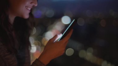 Cep telefonu kullanan ve sosyal medyada bokeh arka planda sohbet eden gülümseyen bir kadının yan görüntüsü