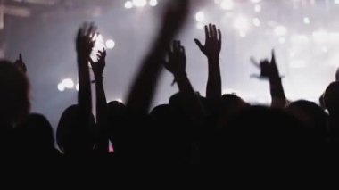 Müzikal performans sırasında siyah ışık sahnesiyle aydınlanmış elleri havada insanların arka plan siluetleri