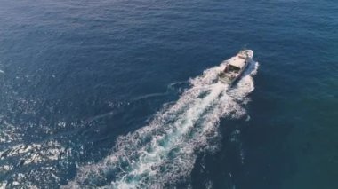 Güneşli bir günde dalgalı deniz suyunda yüzen beyaz motorlu teknenin İHA görüntüsünden