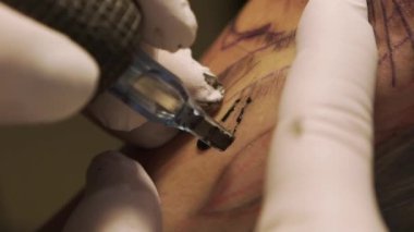 Makina kullanan ve kuaförde siyah mürekkeple dövme yapan yüzsüz dövmecilere yakın çekim.