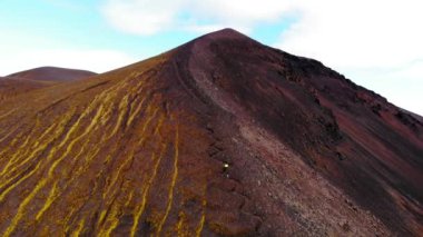 İzlanda 'daki bulutlu gökyüzüne karşı dağ zirvesine çıkan tanınmayan yürüyüşçülerin insansız hava aracı görüntüsünü büyüt
