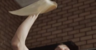 Modern bir restoranda pizza pişirirken mutlu bir adamın hamur fırlatma ve esnetme sahnesini çekiyorum.