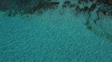 Parlak güneşli bir günde Mallorca adasının kayalık sahillerini yıkayan kristal turkuaz su manzarası.