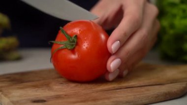Yakın çekim, keskin bıçaklı, taze kırmızı domatesleri tahta kesme tahtasıyla doğrayan anonim ev hanımı ev mutfağında yavaş çekimde yemek hazırlıyor.
